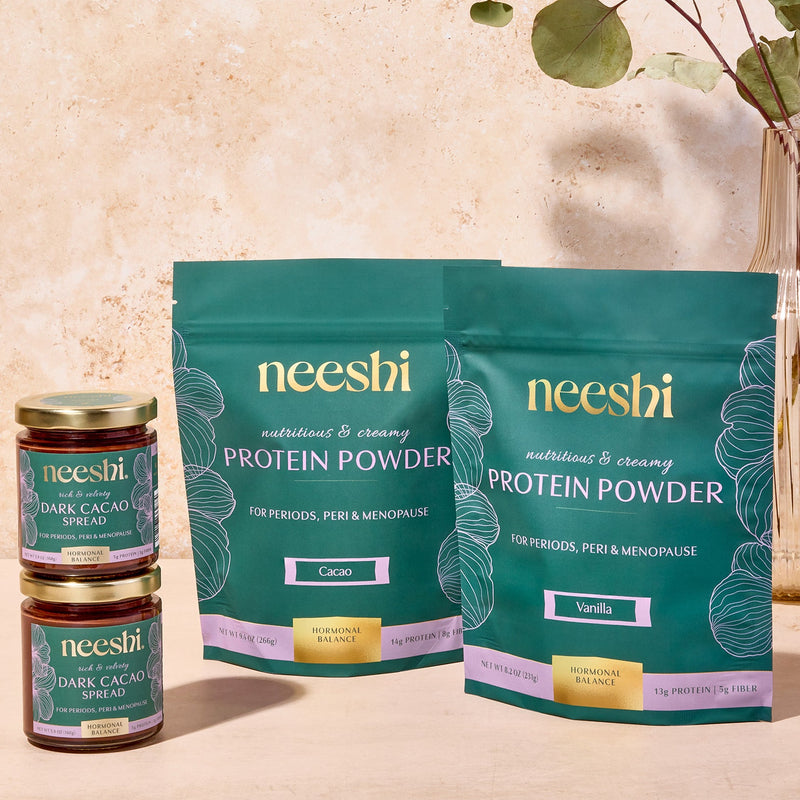 The image displays a selection of health-related products from the brand neesh, including jars of nut butter and pouches of protein powder, arranged on a table with a decorative vase of eucalyptus leaves in the background.