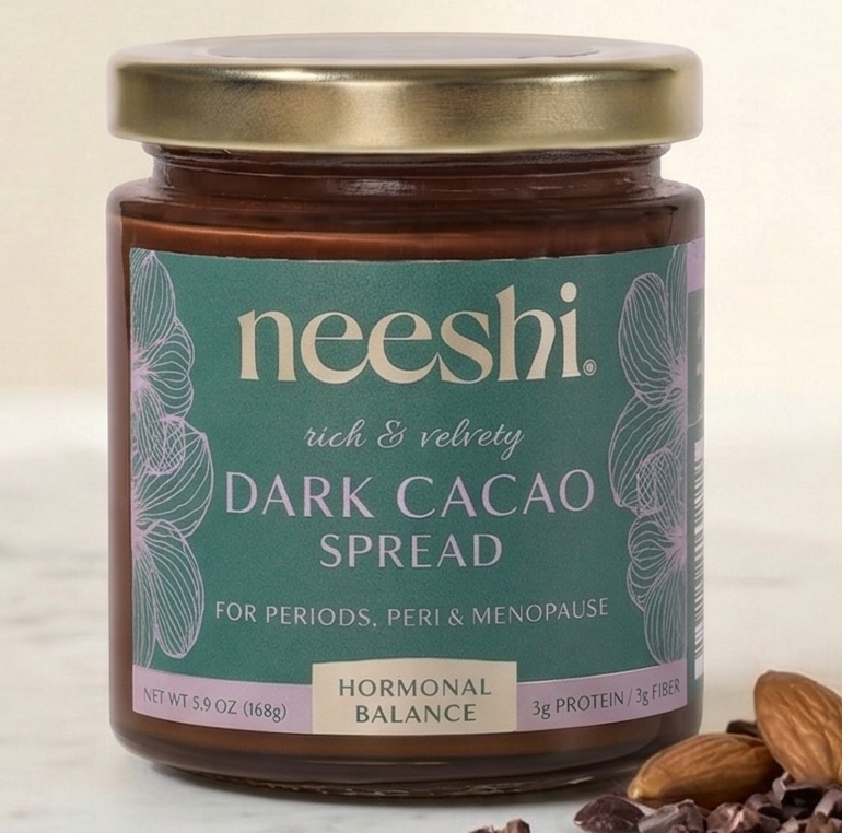 Jar of neeshi dark cacao spread on a marble surface with almonds.