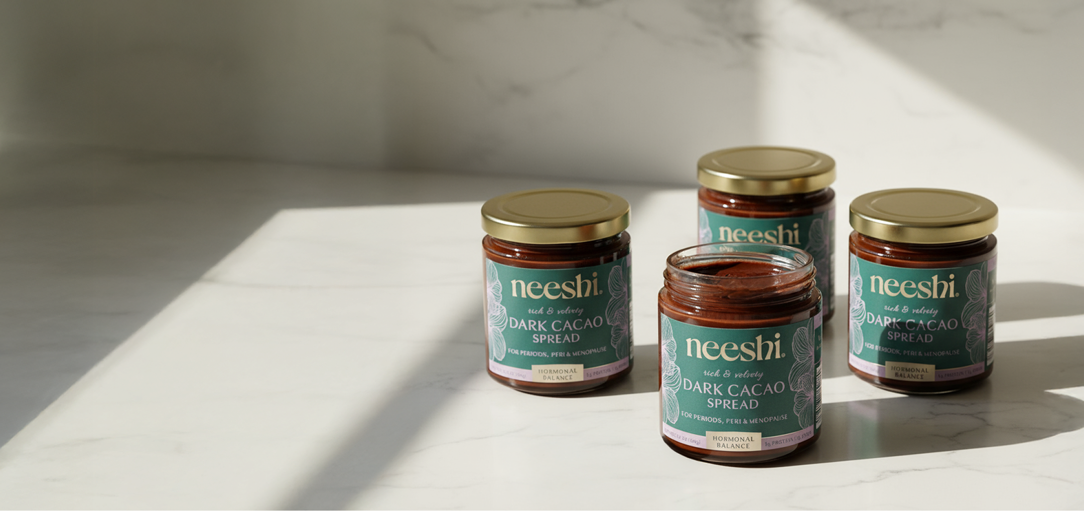 Four jars of neeshi dark cacao spread on a white surface with sunlight casting shadows.