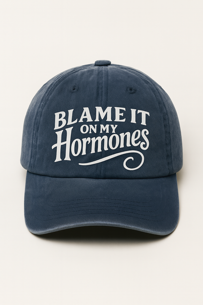Navy blue cap with 'Blame It On My Hormones' text on a white background