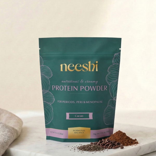 Neeshi protein powder package on a marble surface with cocoa powder.