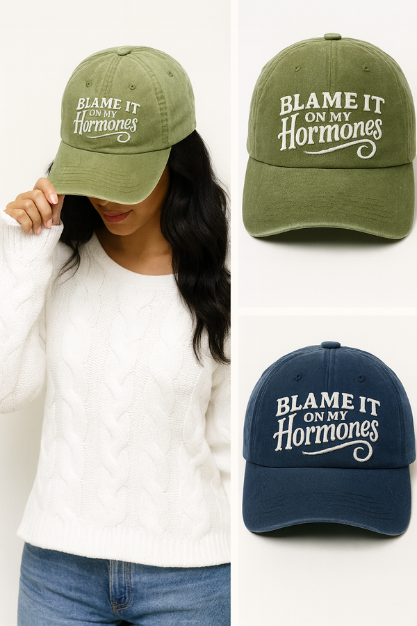 Green and navy baseball caps with 'Blame It On My Hormones' text, worn by a person.