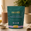 Neeshi protein powder package on a table with a glass of chocolate milk and ingredients.