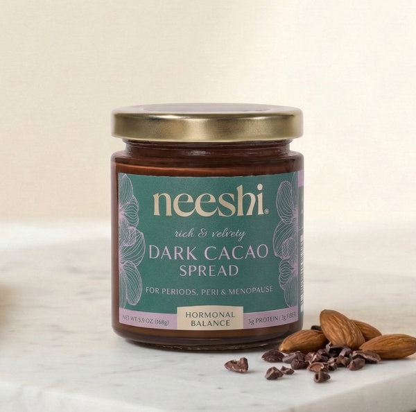 Jar of neeshi dark cacao spread on a marble surface with almonds.